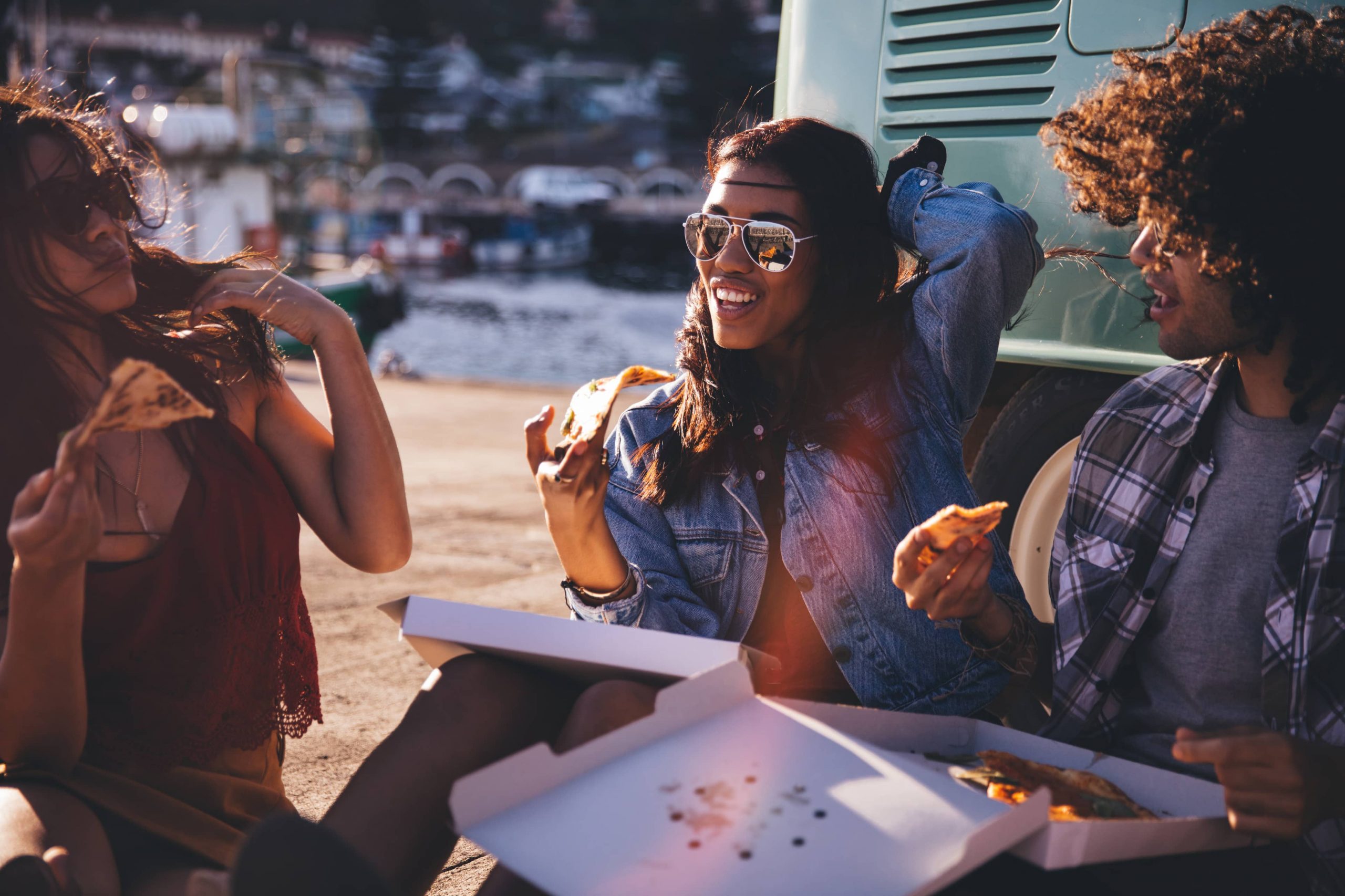three people sharing a take-away pizza on the beach