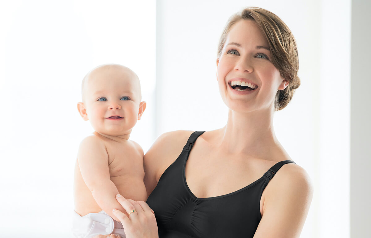 A woman holding a baby, both smiling at the camera.