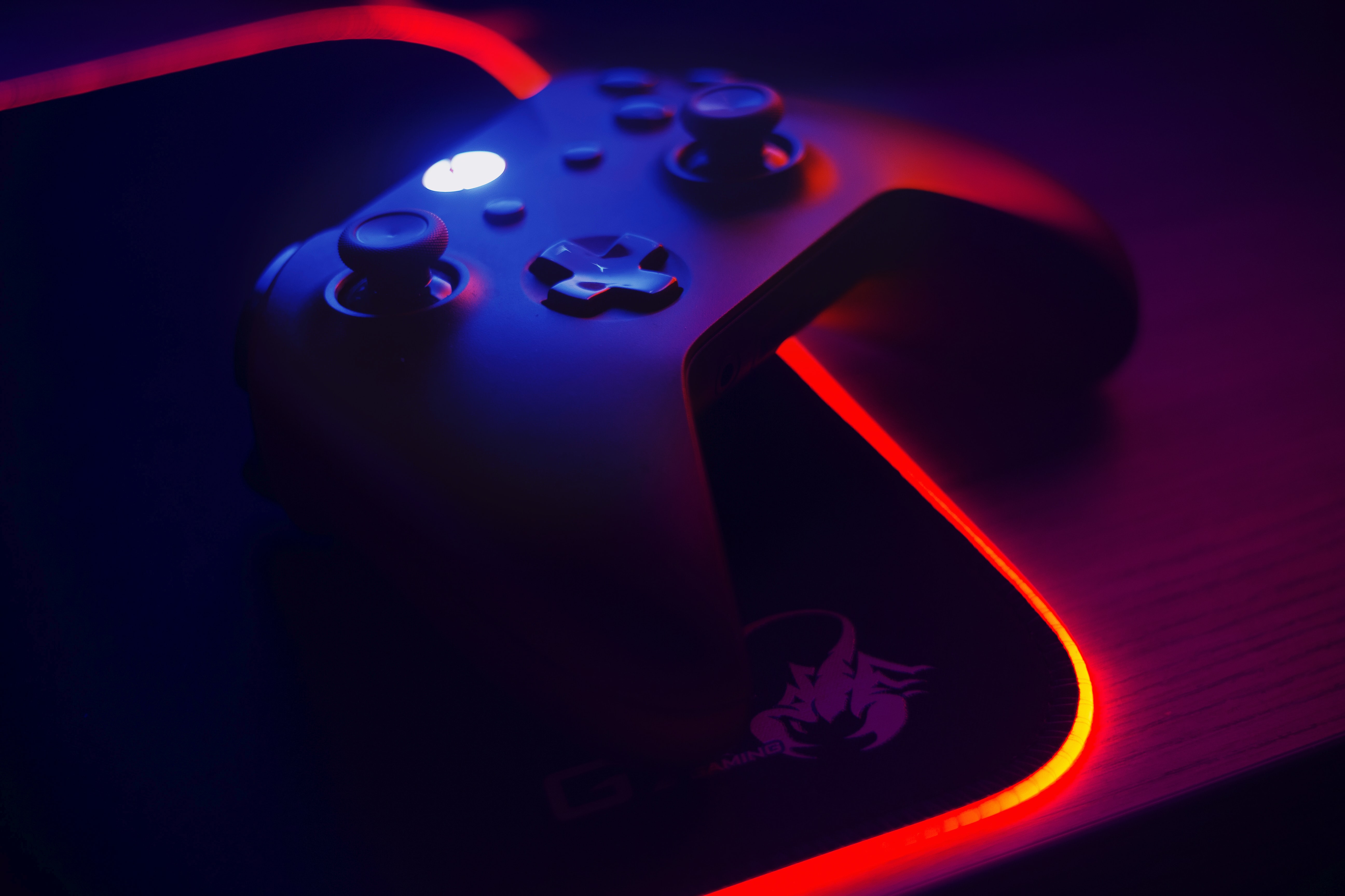 An Xbox controller on a dark desk, illuminated by neon light.