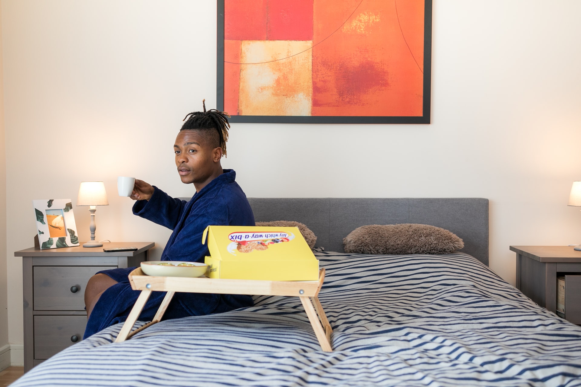 Man sitting on bed with coffee in hand.