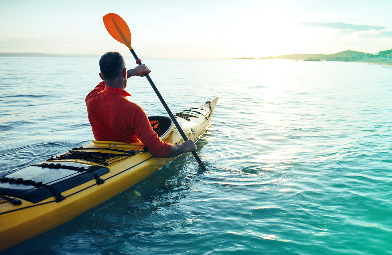 Senior man paddling kayak on the sunset sea