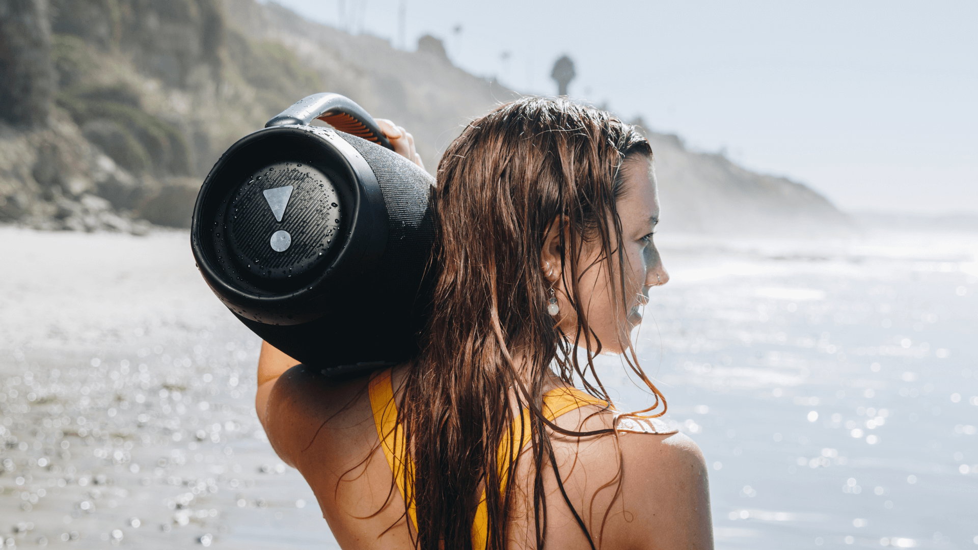 woman holding JBL speaker on beach