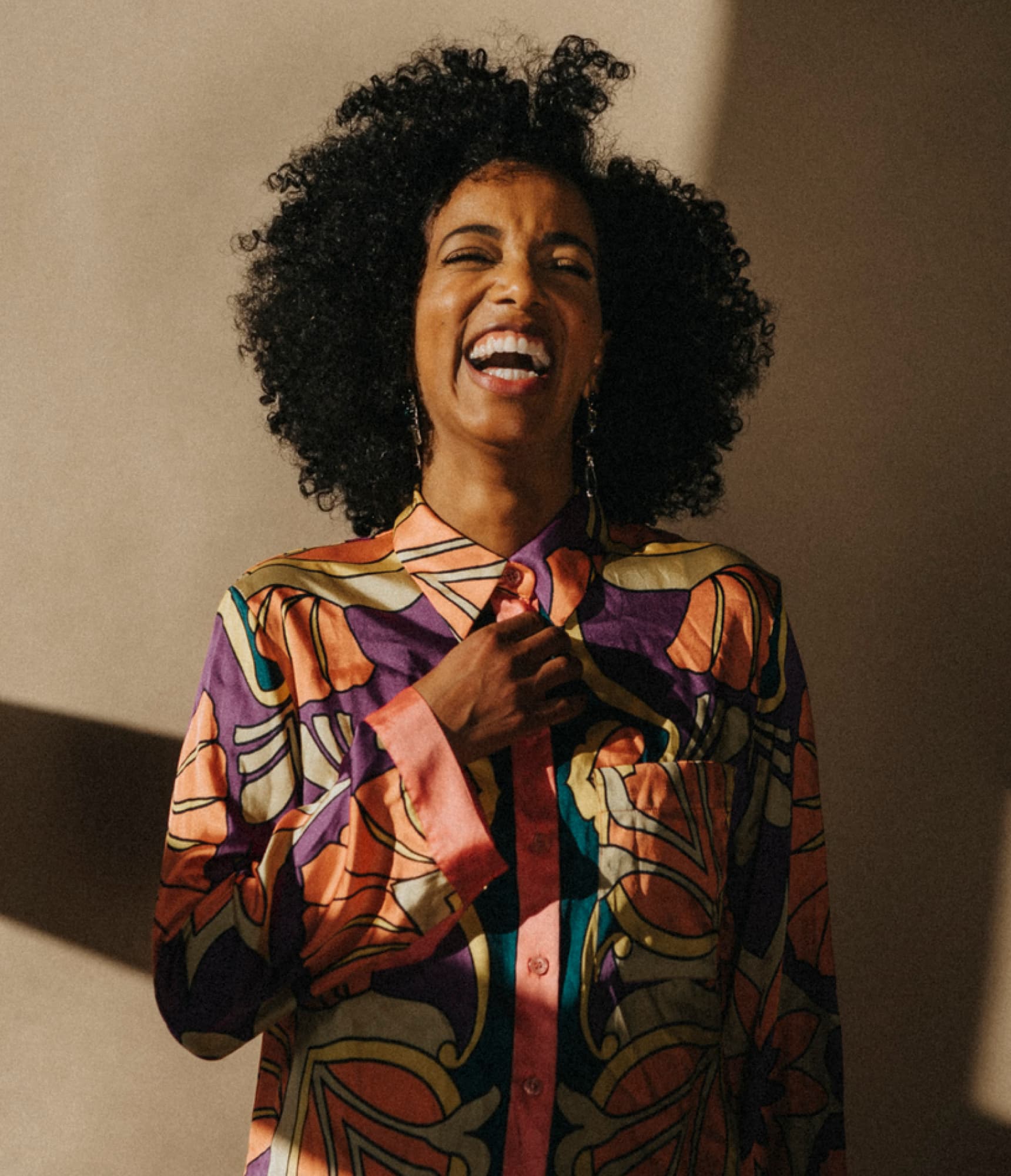 Woman laughing with her hand on her chest against a beige backdrop