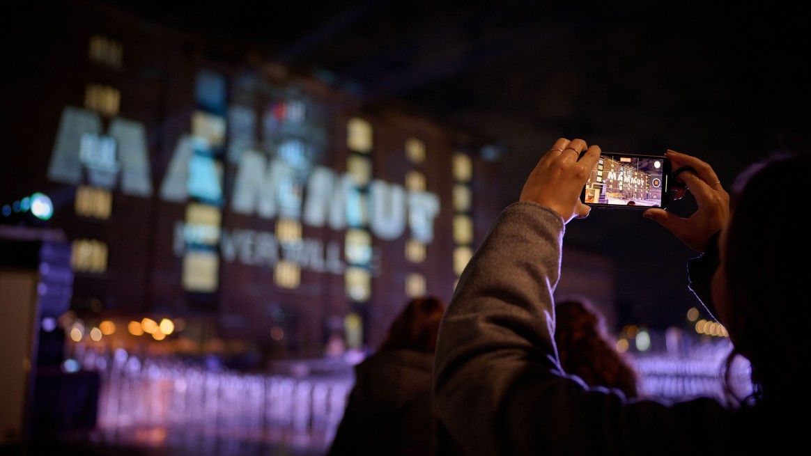 Man taking a photo of a building with the Mammut logo projected onto it