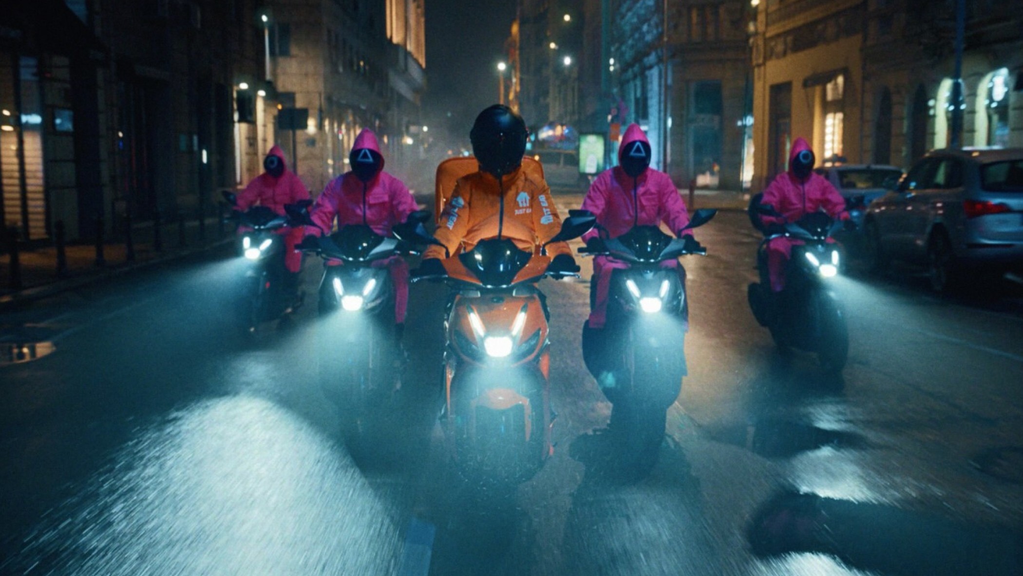 Just eat delivery driver on a motorcycle with five men in pink jumpsuits riding on motorcycles behind him