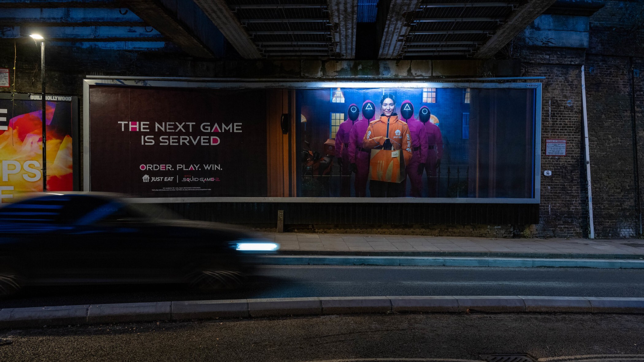 billboard of woman food delivery driver in orange jacket holding a just eat delivery bag with four men in pink jumpsuits behind her