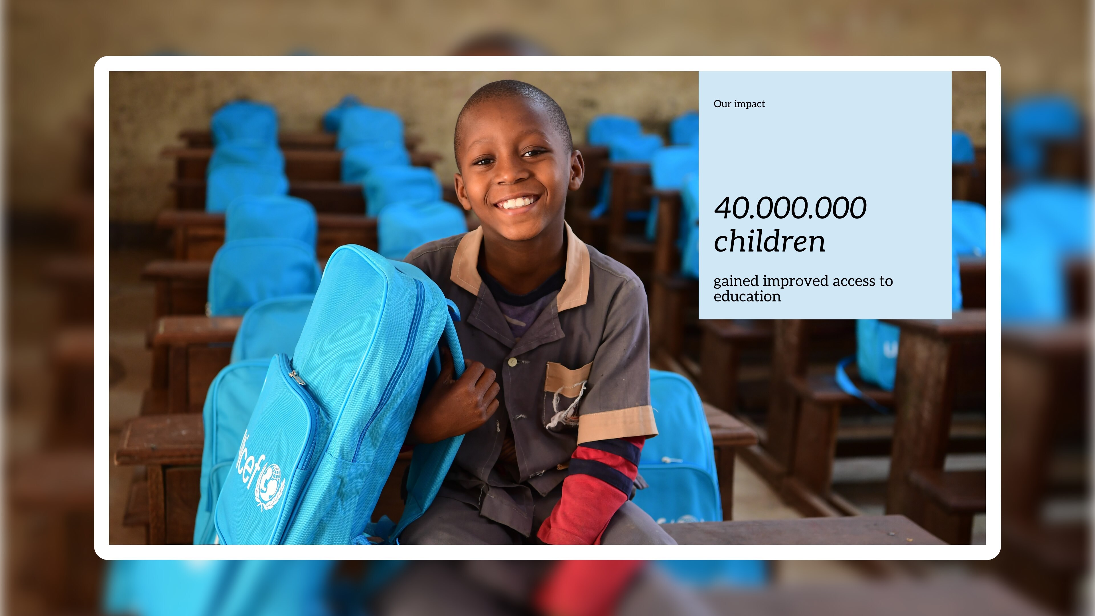 smiling boy sitting in empty classroom with a blue Unicef backpack
