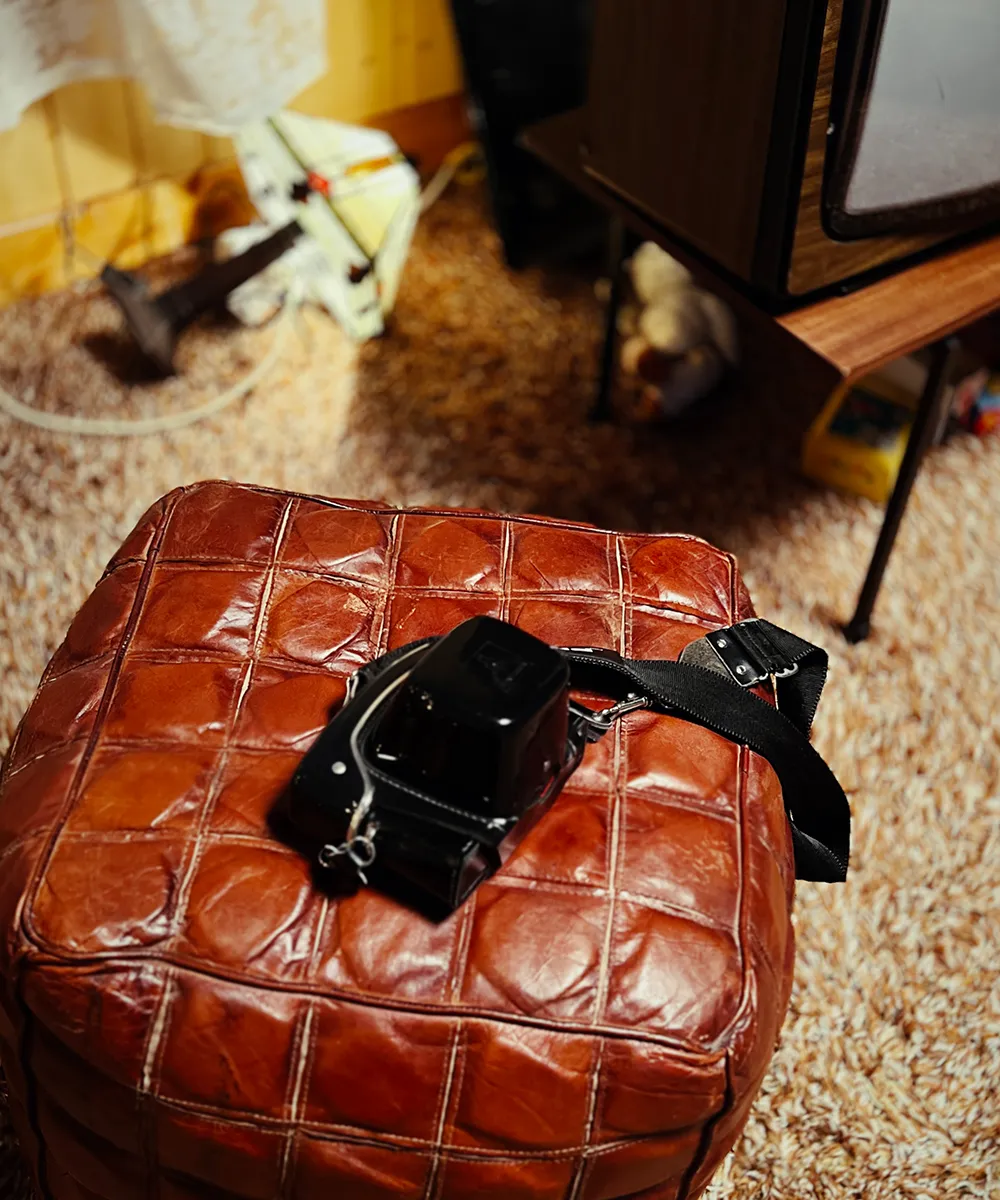 A black vintage camera resting on a tufted brown leather ottoman over a shag rug.
